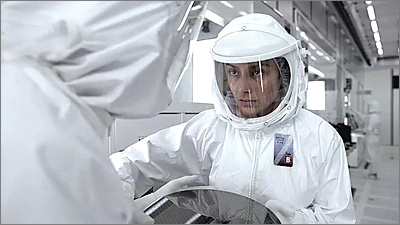 Still frame from Apple's new Intel TV commercial, showing a woman in a white clean room suit taking a large silicon wafer from a colleague.