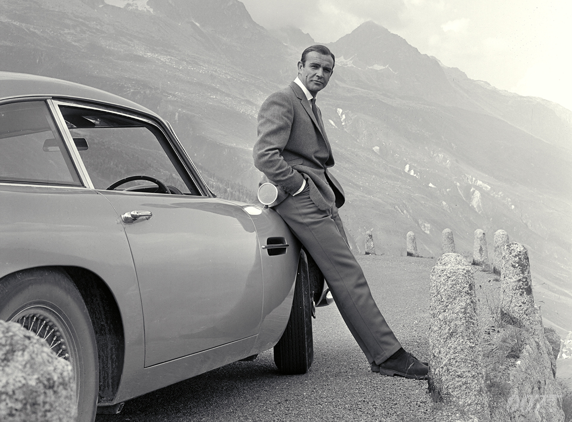 Sean Connery, as James Bond, leaning against an Aston Martin DB5.