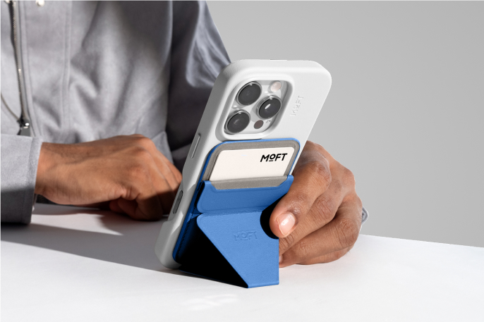 A blue Moft Snap-On iPhone Stand, propping an iPhone vertically.